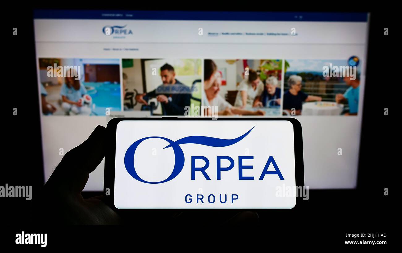 Persona che tiene uno smartphone con il logo della casa di cura francese Orpea S.A. sullo schermo di fronte al sito web. Mettere a fuoco sul display del telefono. Foto Stock