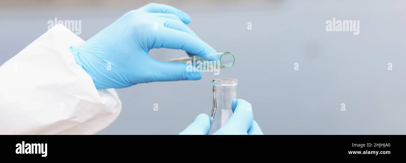 Lo scienziato in guanti e tuta protettiva versa l'acqua sporca dalla provetta al pallone Foto Stock
