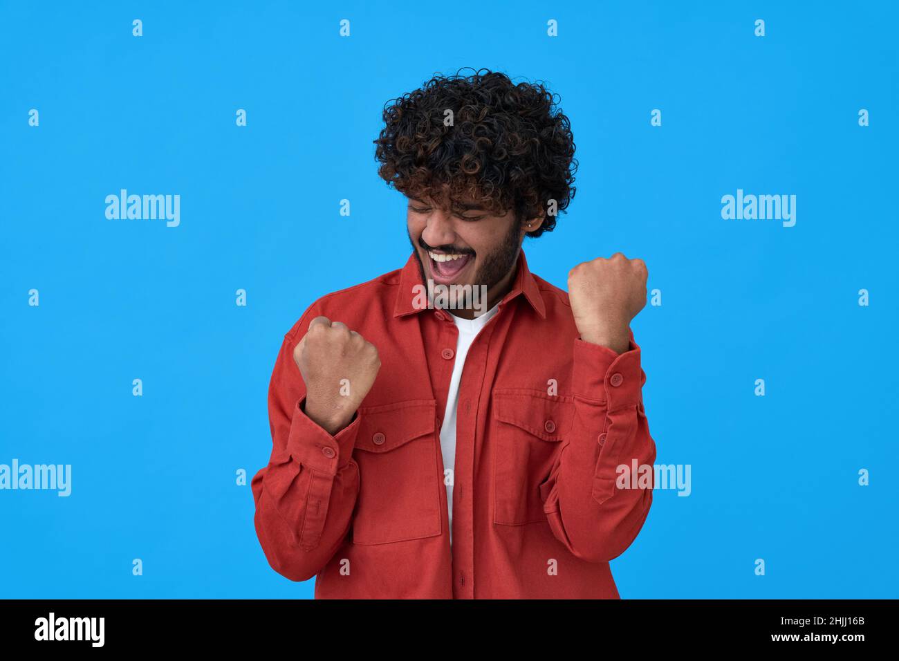 Il giovane vincitore indiano eccitato festeggia la vittoria isolata su sfondo blu. Foto Stock