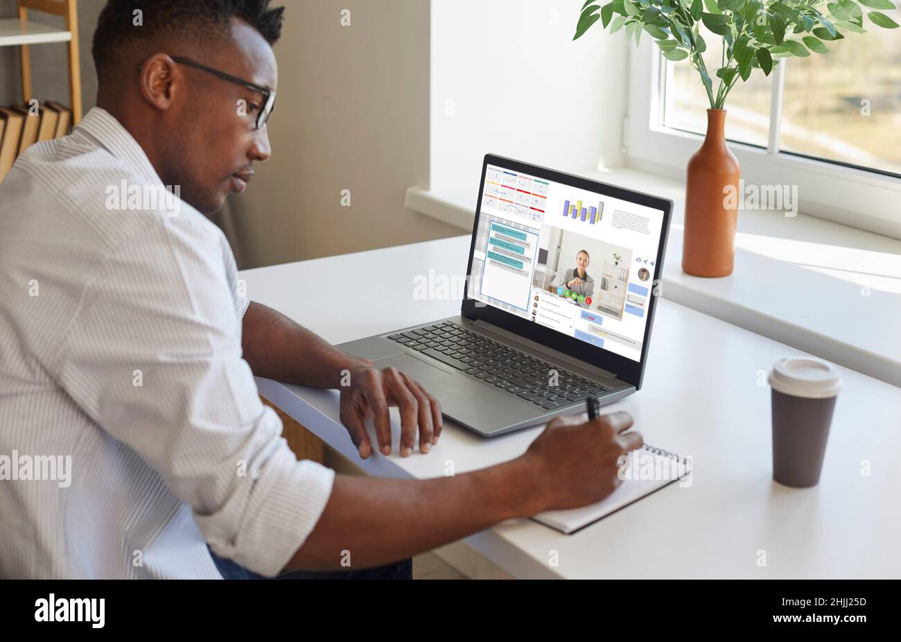 Uomo nero che lavora sul laptop, comunica tramite chat e videochiamata e prende appunti Foto Stock
