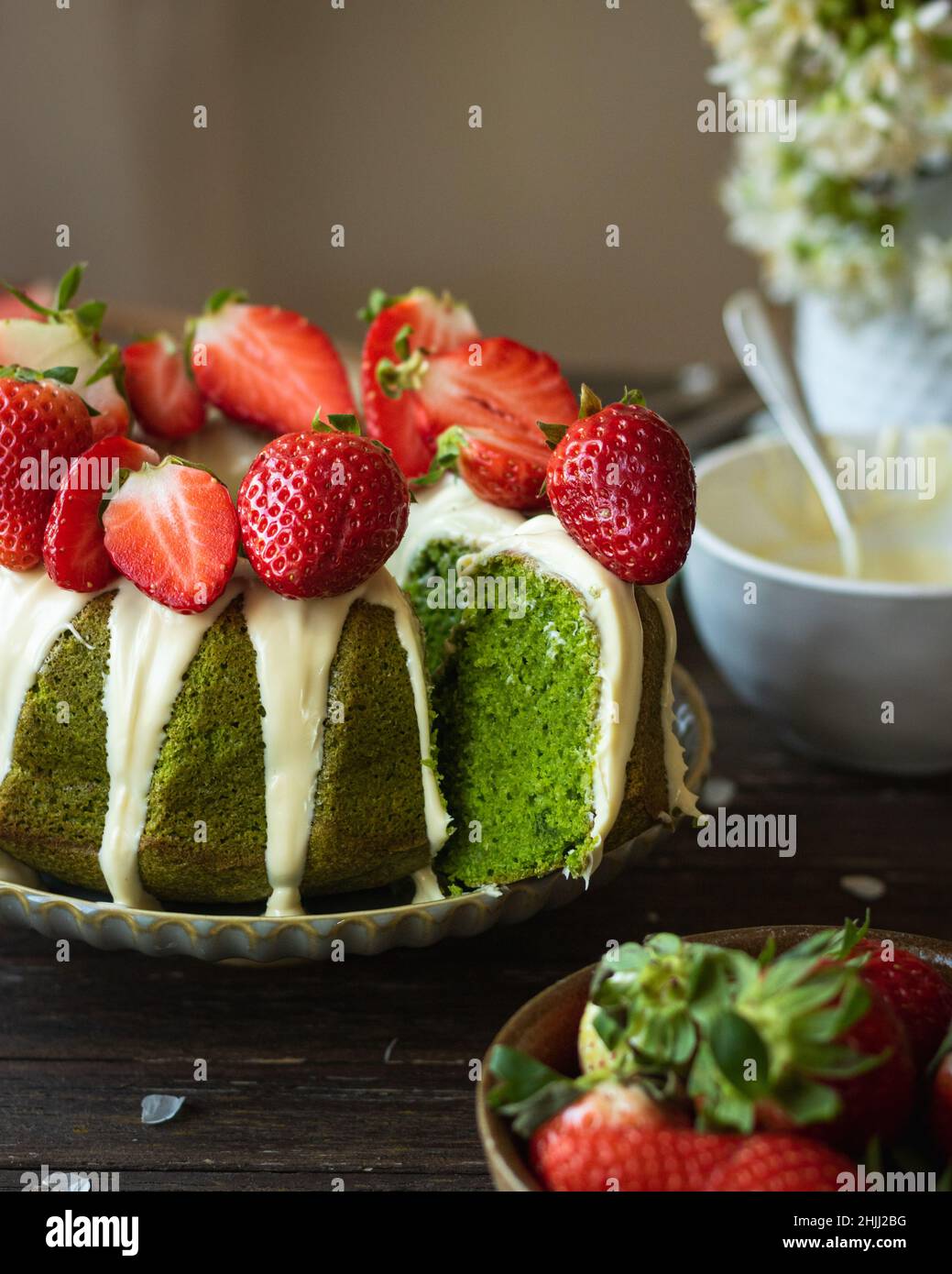Torta di spinaci verdi con fragola su sfondo rustico scuro in legno. Ragazza in abito bianco che si glassa sulla torta. Primavera ancora vita Foto Stock