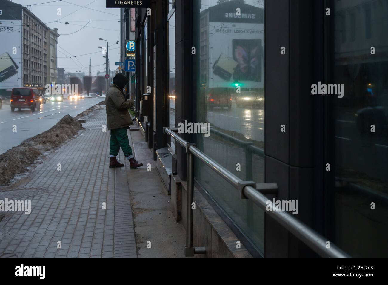 Riga, Lettonia, 4 gennaio 2022: Vista della città con auto di passaggio e un uomo con uno smartphone allo stand sigarette Foto Stock