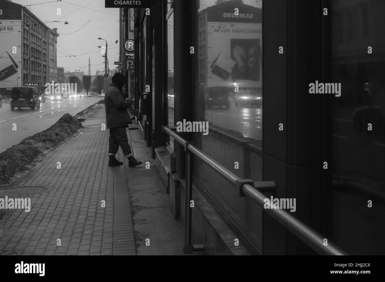 Riga, Lettonia, 4 gennaio 2022: Vista della città con auto di passaggio e un uomo con uno smartphone allo stand sigarette Foto Stock
