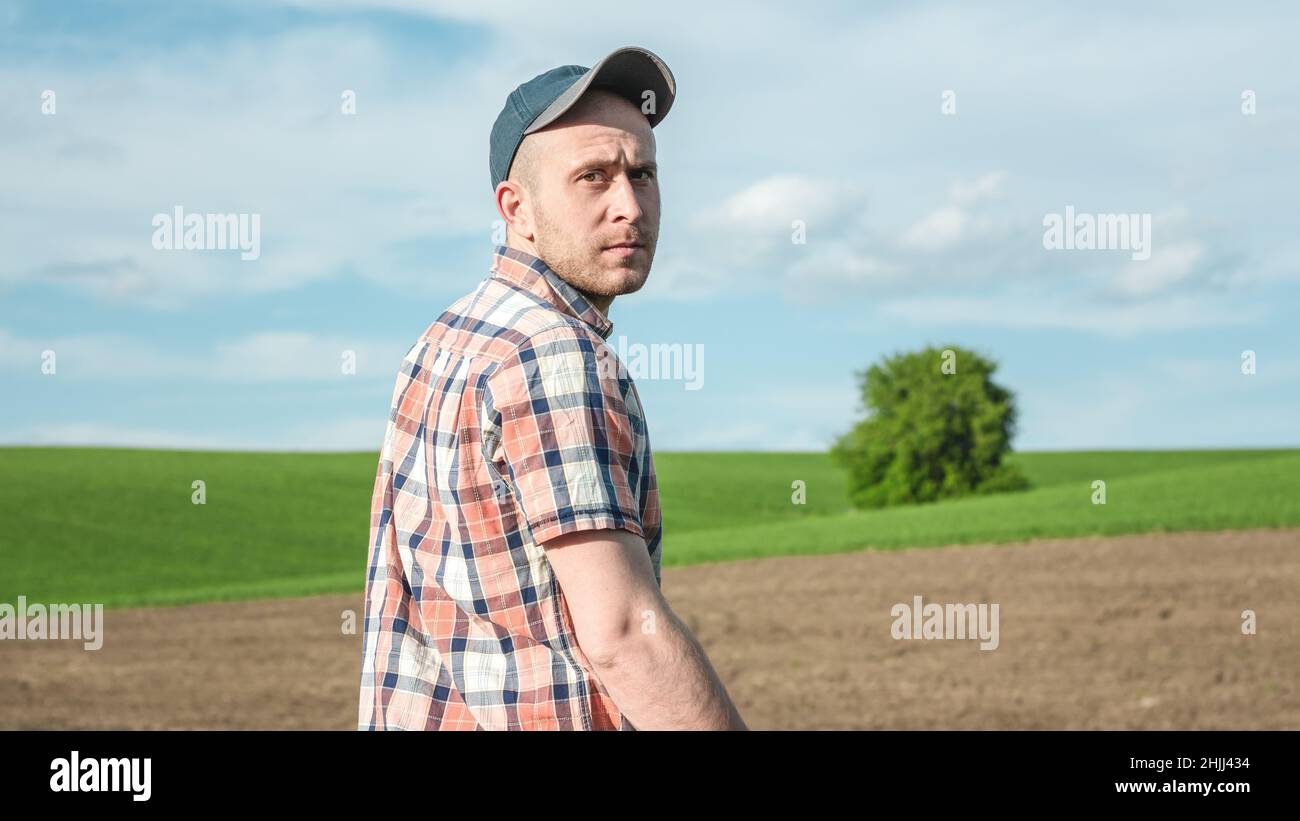 Ritratto di un agronomo maschile che ispeziona le colture di grano in un campo agricolo. Coltivatore in un campo di grano. Valutazione della resa del raccolto di grano Foto Stock