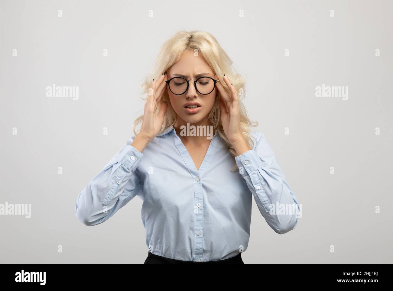 Giovane imprenditore stanco femminile che soffre di mal di testa e templi toccanti, in piedi su sfondo studio chiaro Foto Stock