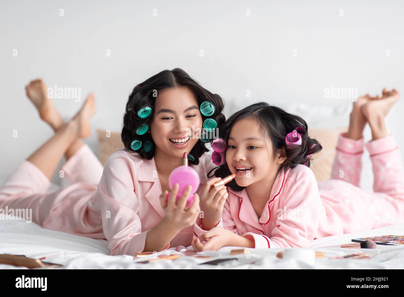 Allegra signora giapponese millenaria con curlers tenere specchio per  ragazza teen, applicare rossetto sulle labbra, sul letto con cosmetici Foto  stock - Alamy