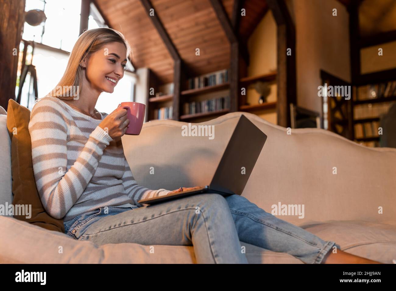 Donna sorridente che usa il laptop a casa, bevendo caffè Foto Stock