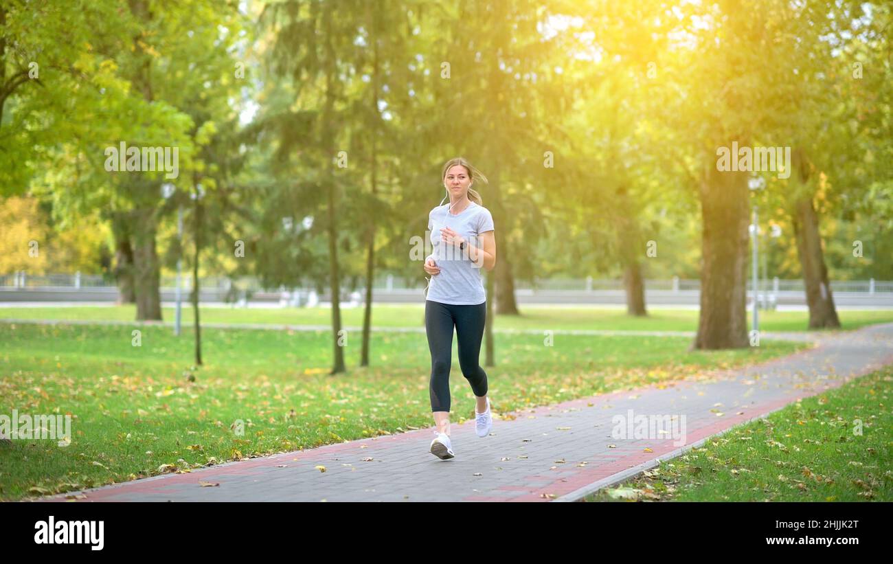 L'atleta si allena nel parco all'alba. L'atleta corre lungo la pista, ascolta la musica con le cuffie. Stile di vita sano. Foto Stock