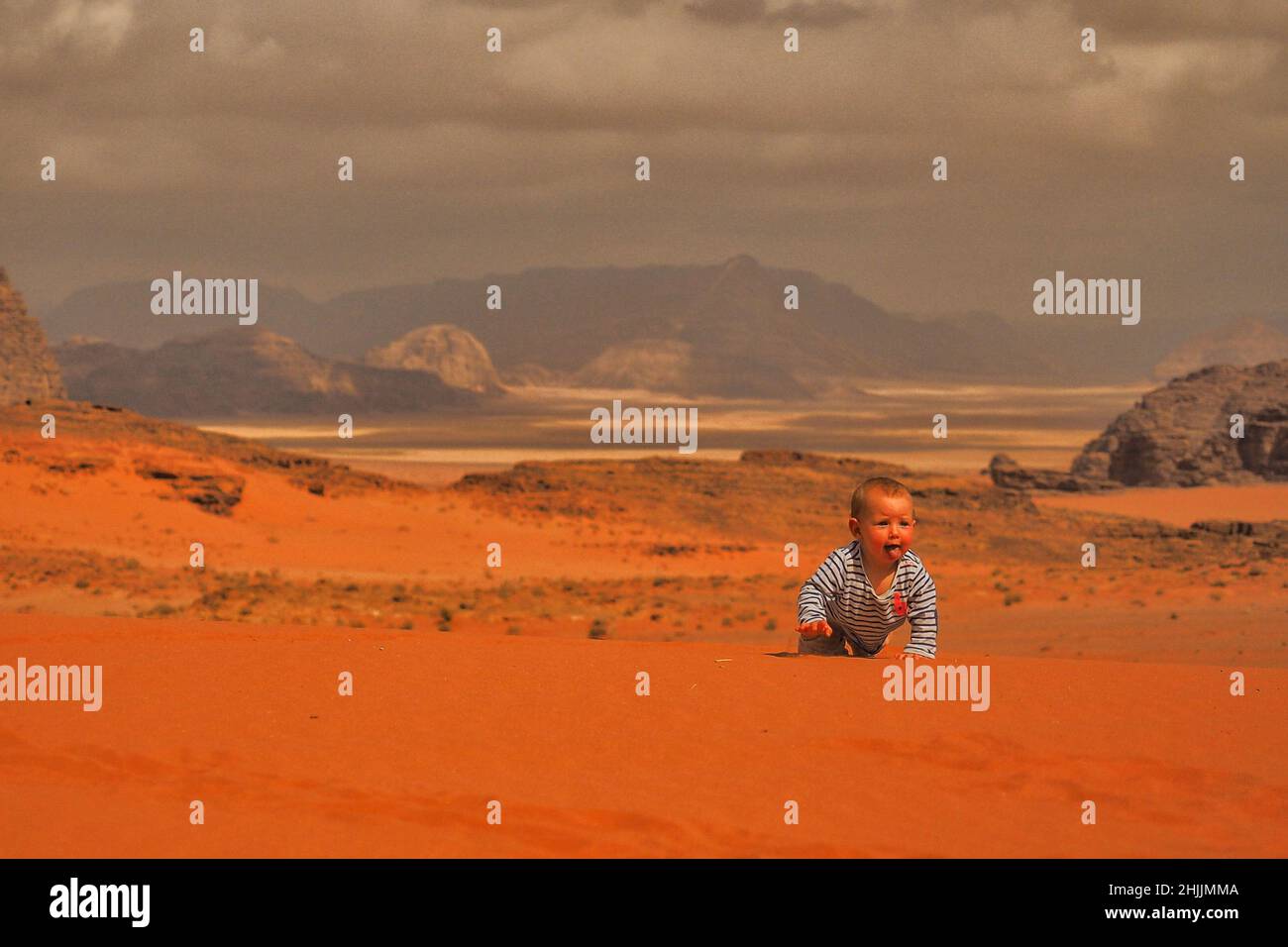 Una bambina carina che striscia su una sabbia. Deserto e montagne di Wadi Rum, Giordania. Foto Stock