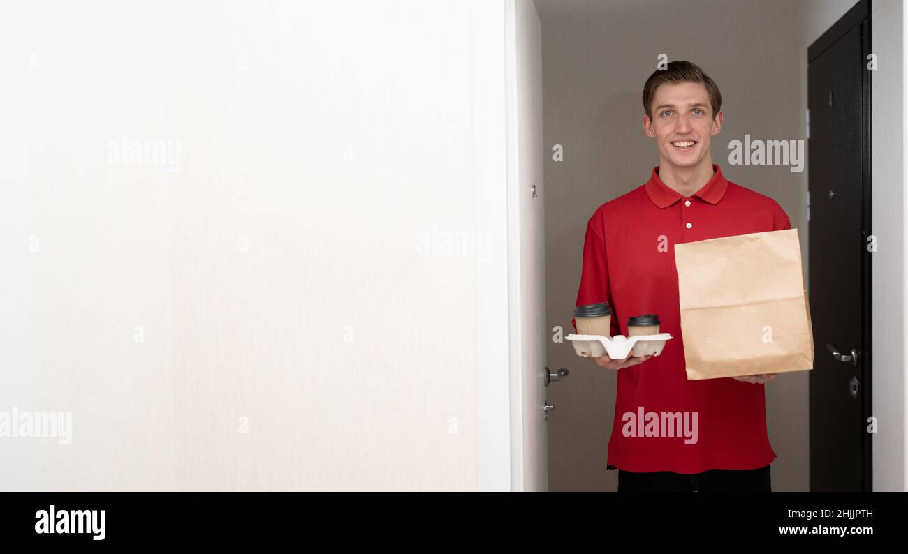 consegna a casa di cibo e caffè, consegna a domicilio con pacchetto ecologico e bicchieri americano a portata di mano, corriere in uniforme rossa ordinando cibo takeaway Foto Stock