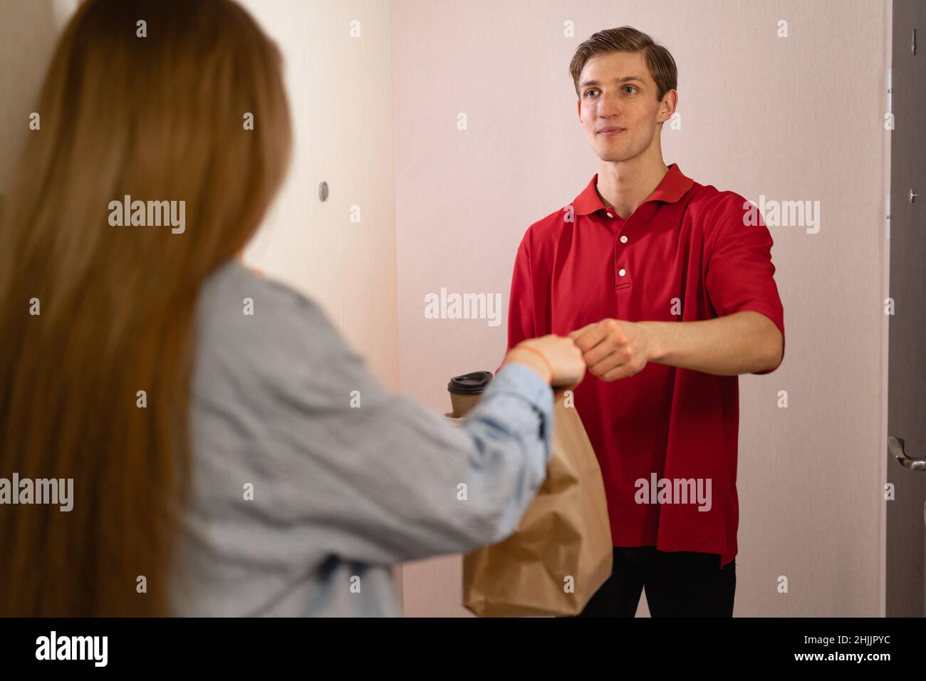 Concetto di consegna del cibo. Deliveryman che consegna un pacchetto di un ordine al cliente. Servizio di consegna cibo da asporto. Il cliente riceve il pacchetto eco Foto Stock