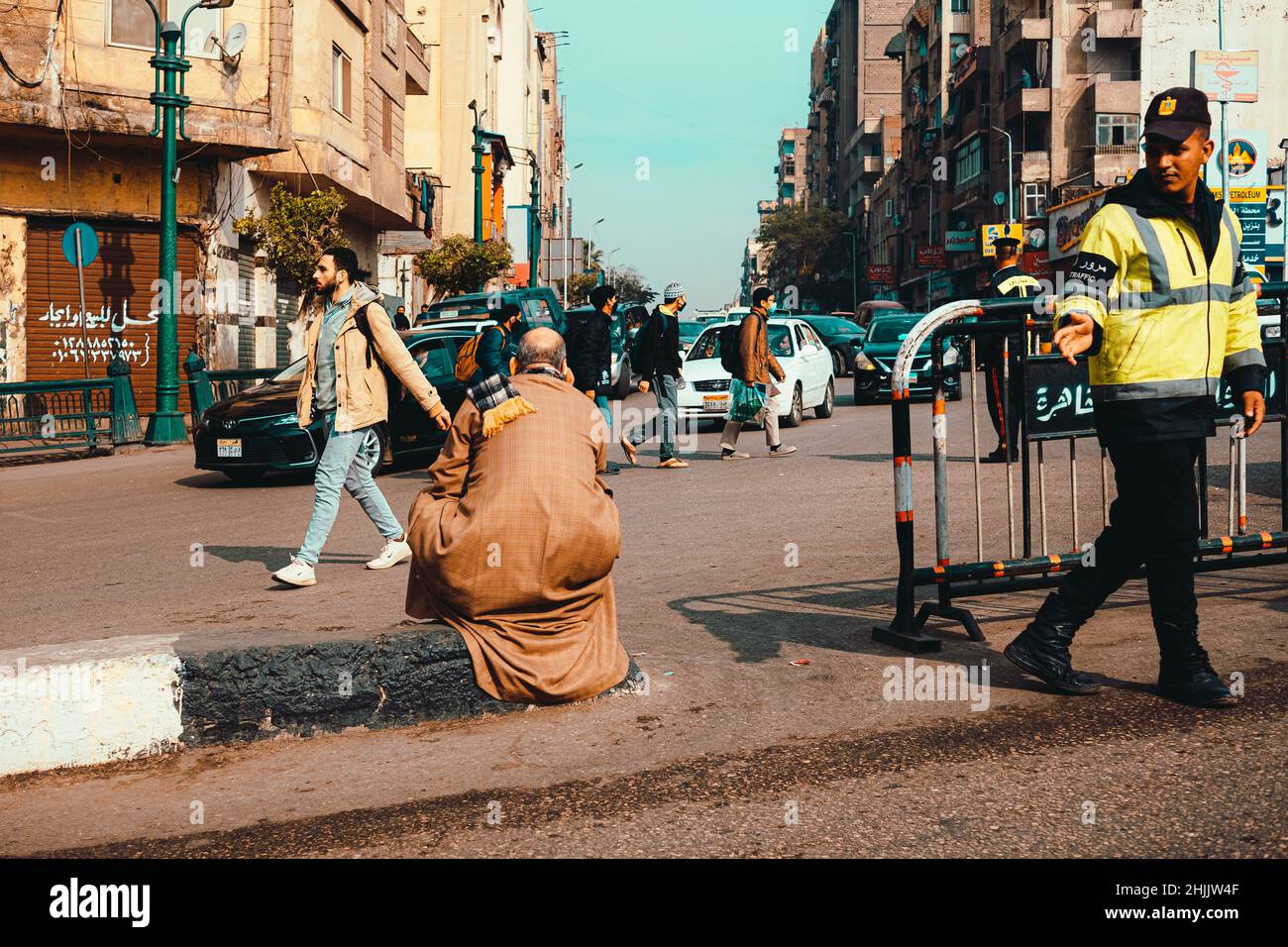 Cairo Egitto Dicembre 2021 scena occupato nel centro del cairo, giovane ufficiale di polizia che dirige il traffico mentre un vecchio si siede nel mezzo della strada Foto Stock