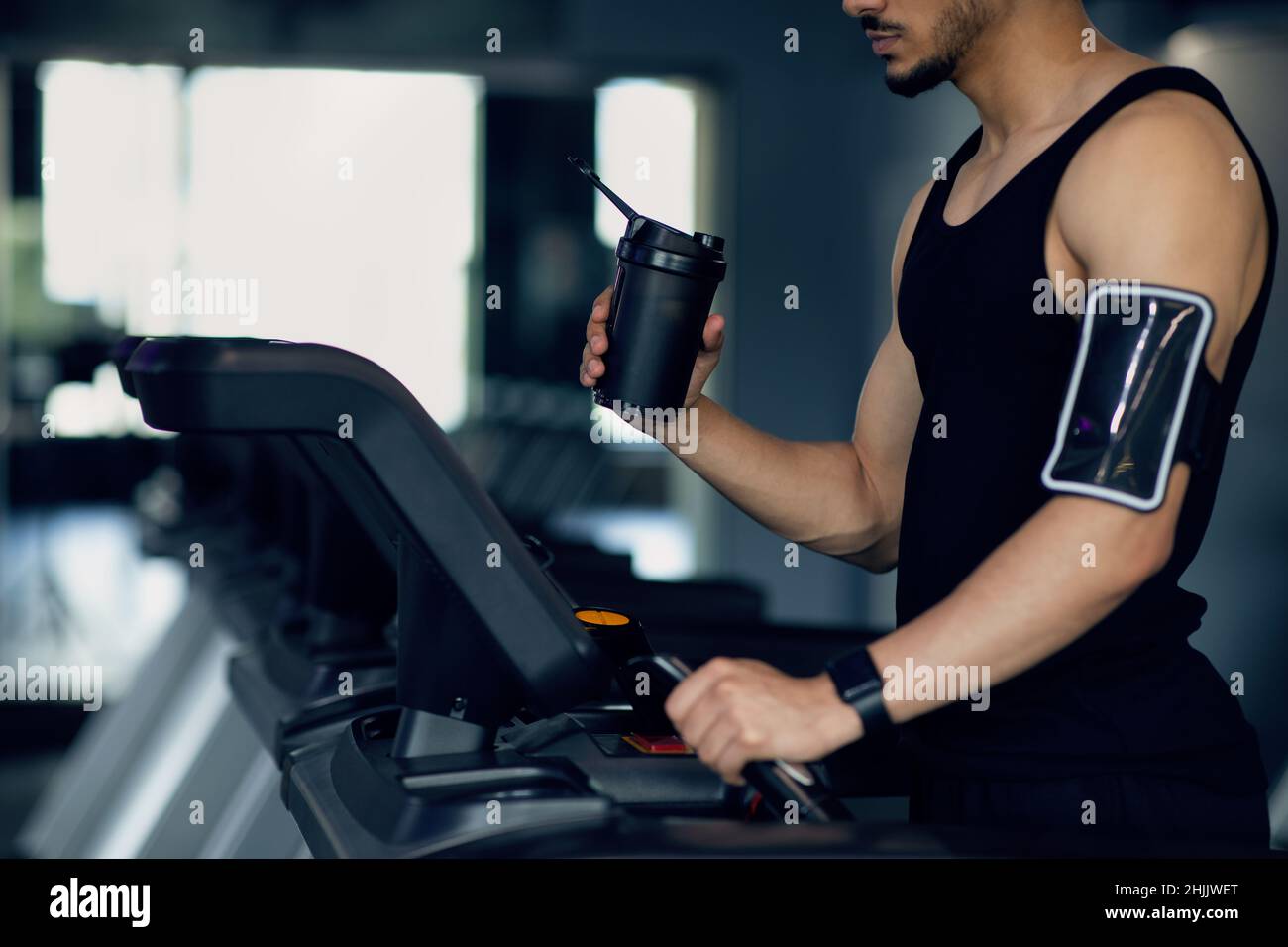 Atleta maschile con Sport Shaker e fascia da braccio telefonica con tapis roulant in palestra Foto Stock