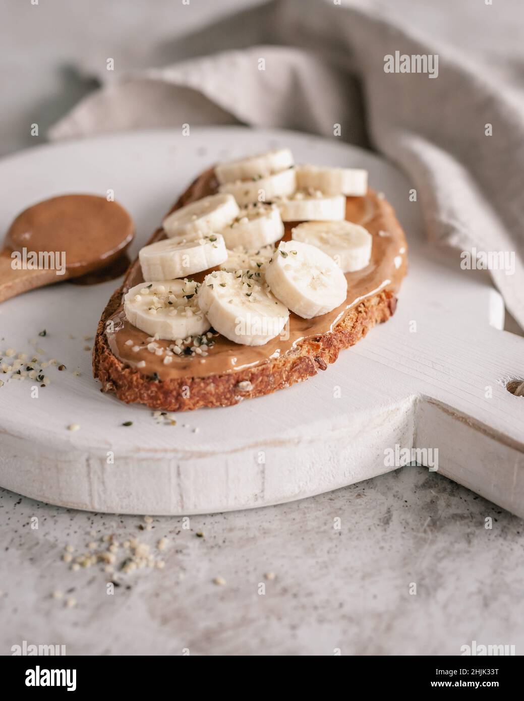 Affettare il pane di pasta madre con burro di arachidi, banana e semi di canapa su un tagliere Foto Stock