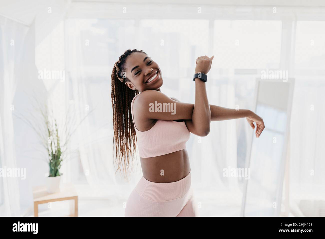 Ritratto di attraente fit afroamericana signora in abbigliamento sportivo che si esercita a casa, allungando il braccio e sorridendo alla macchina fotografica Foto Stock