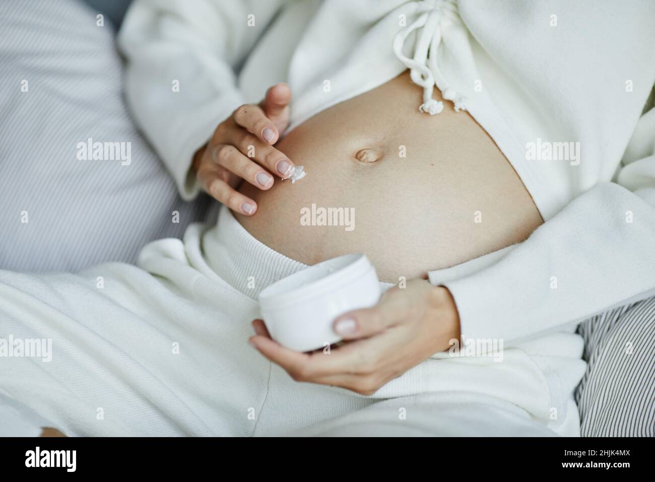 Primo piano di una giovane donna incinta che applica crema anti-stretch sul ventre durante la gravidanza Foto Stock