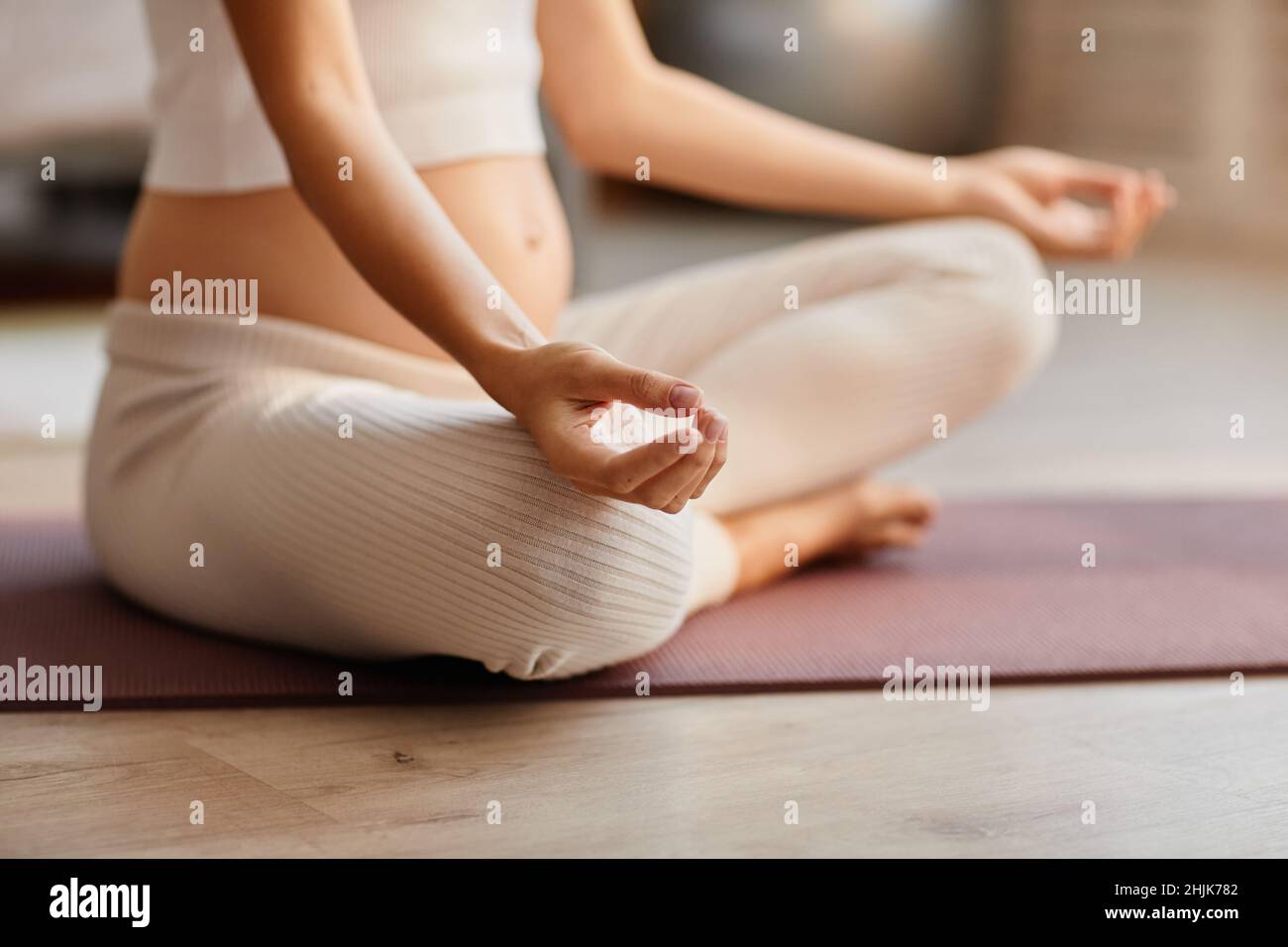 Primo piano di una giovane donna incinta seduta su materassino da sforzo e meditating durante il suo addestramento Foto Stock