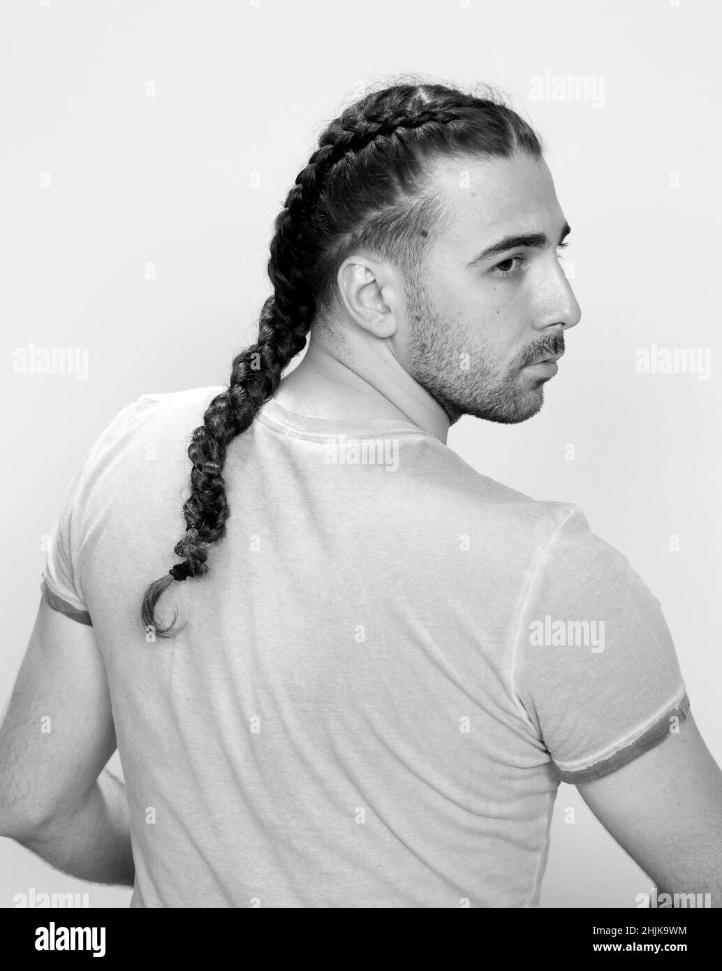 Modello maschile elegante con trecce in posa in studio su sfondo isolato. Stile, acconciatura, concetto di moda. Foto Stock