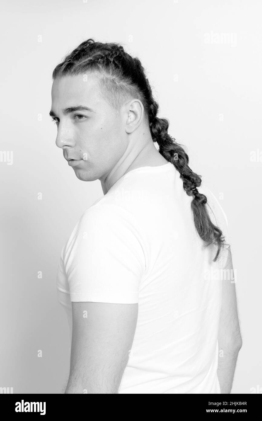 Modello maschile elegante con trecce in posa in studio su sfondo isolato. Stile, acconciatura, concetto di moda. Foto Stock