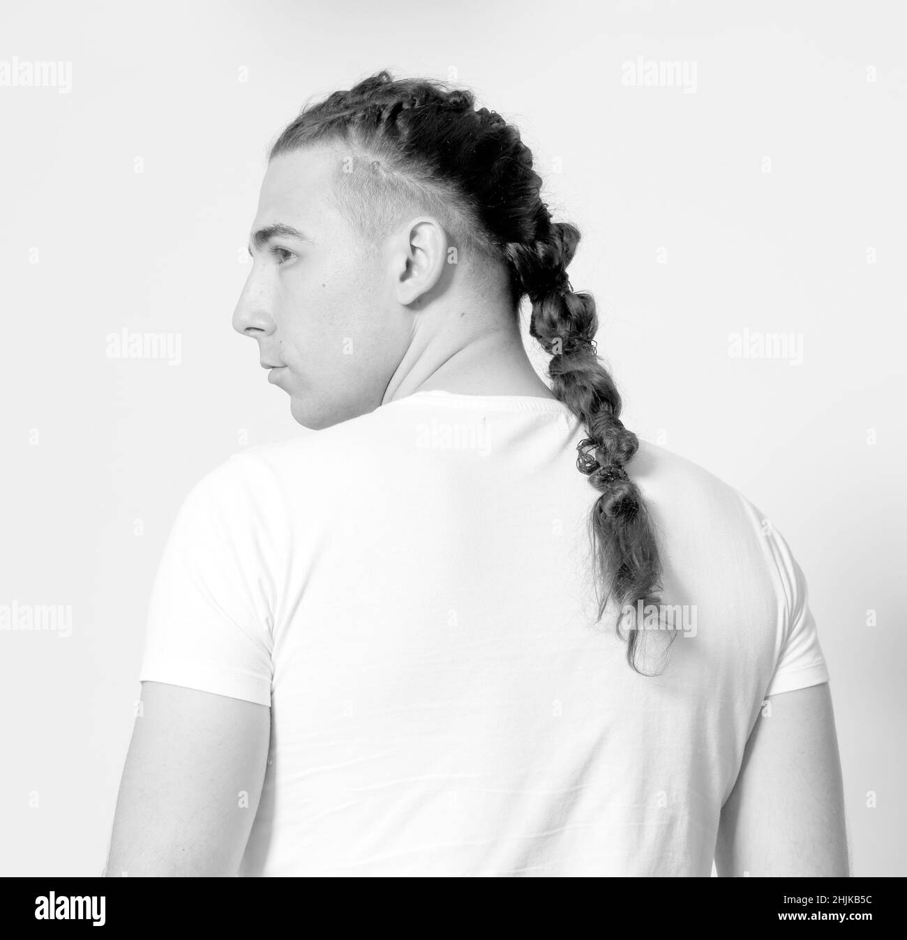 Modello maschile elegante con trecce in posa in studio su sfondo isolato. Stile, acconciatura, concetto di moda. Foto Stock