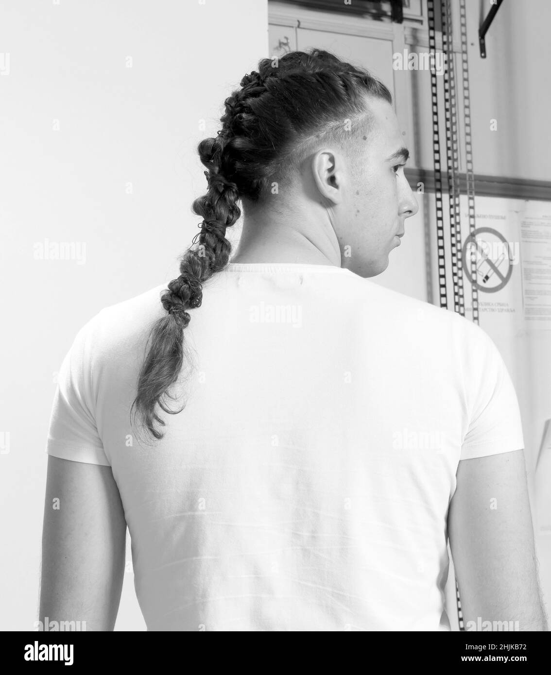 Modello maschile elegante con trecce in posa in studio su sfondo isolato. Stile, acconciatura, concetto di moda. Foto Stock