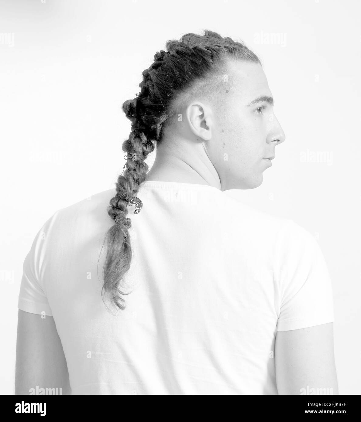 Modello maschile elegante con trecce in posa in studio su sfondo isolato. Stile, acconciatura, concetto di moda. Foto Stock