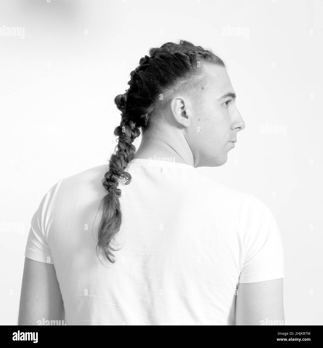 Modello maschile elegante con trecce in posa in studio su sfondo isolato. Stile, acconciatura, concetto di moda. Foto Stock