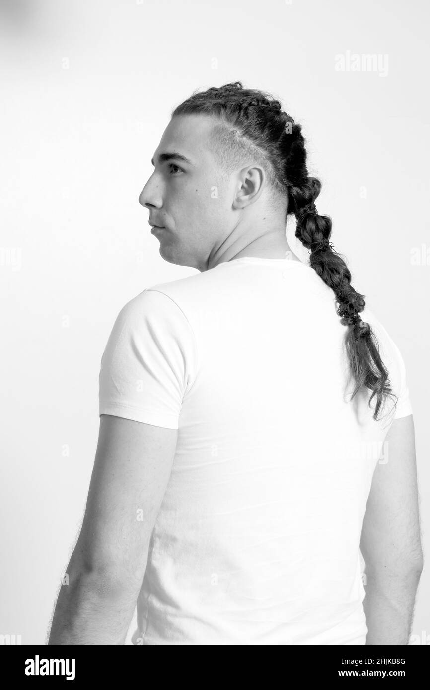 Modello maschile elegante con trecce in posa in studio su sfondo isolato. Stile, acconciatura, concetto di moda. Foto Stock