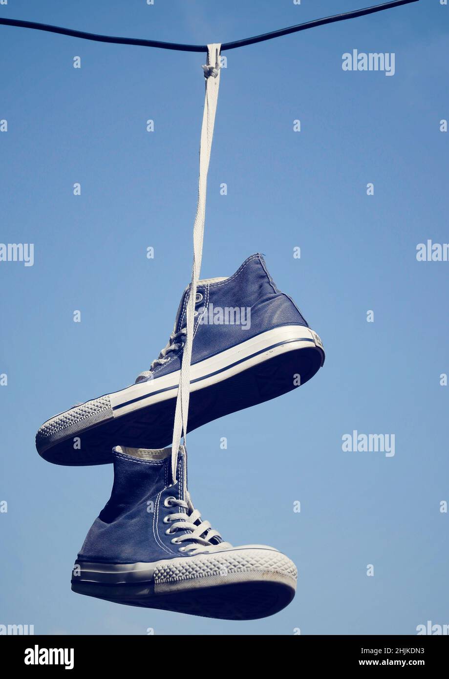 Vecchie sneakers appese su un cavo elettrico su uno sfondo cielo chiaro Foto Stock