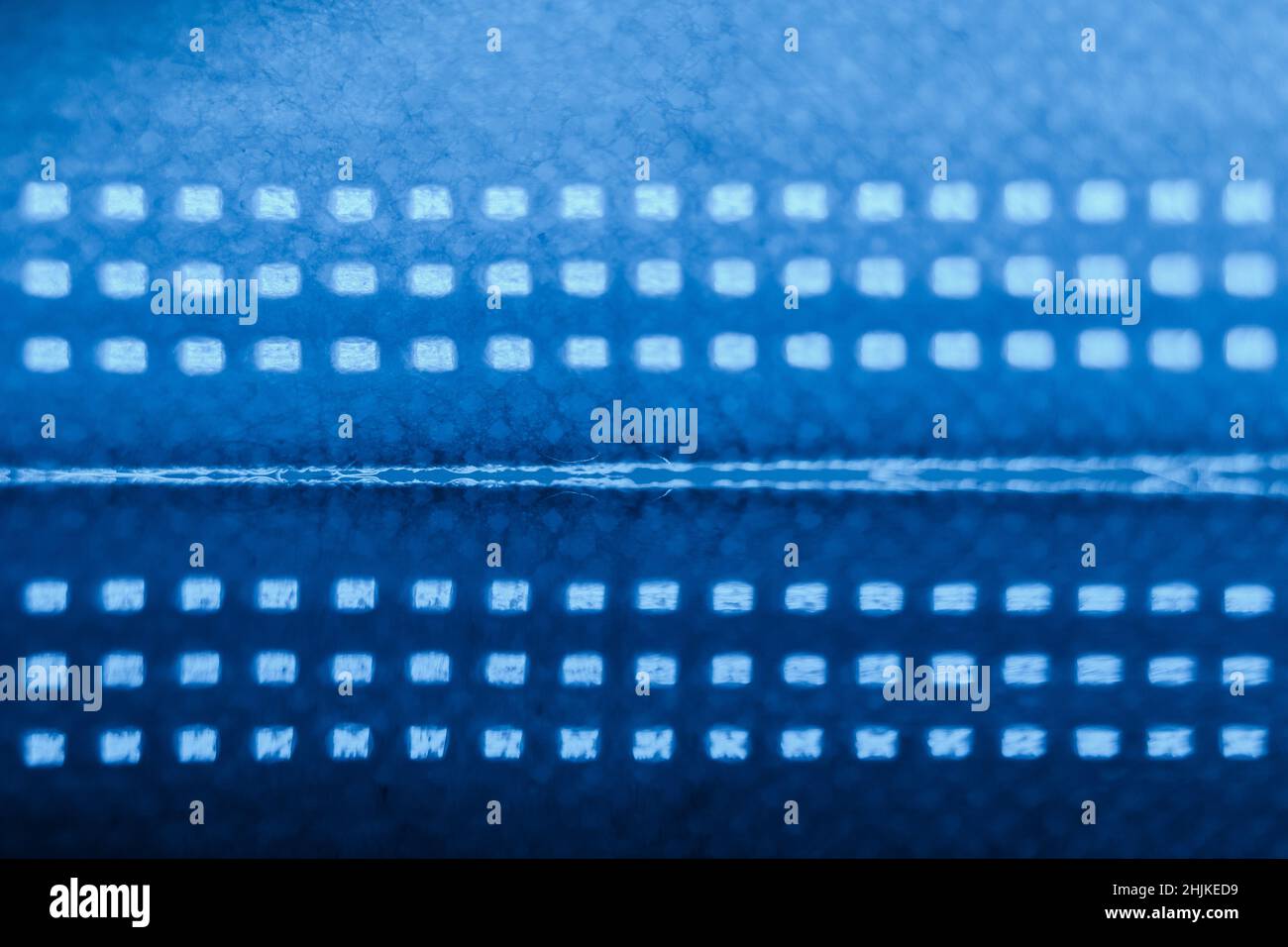 Sfondo scuro e ultramarino composto da dettagli della maschera chirurgica su una superficie riflettente. Foto Stock