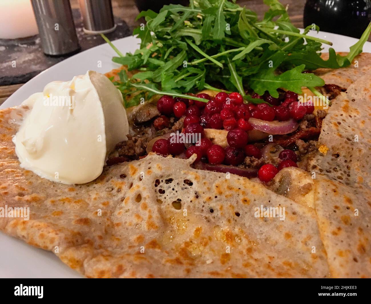 Una crepe o una galette farcita di carne fritta, funghi, lingonberry, cazzata di rucola e creme fraiche Foto Stock