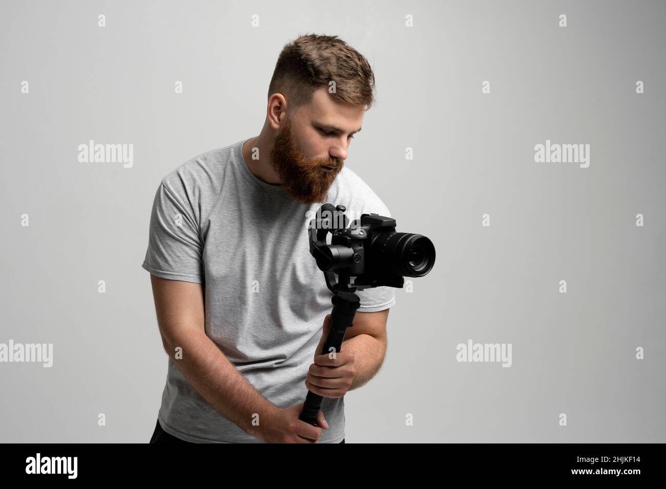 Filmmaking, hobby e concetto di creatività. Videografo maschile professionale che realizza video utilizzando la moderna fotocamera reflex digitale su una parete bianca con sospensione cardanica a 3 assi. Foto Stock