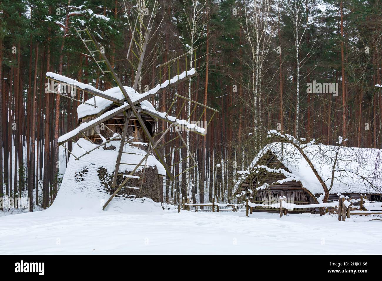 Vecchia casa di legno e mulino a vento coperto di neve in una foresta invernale. Foto Stock