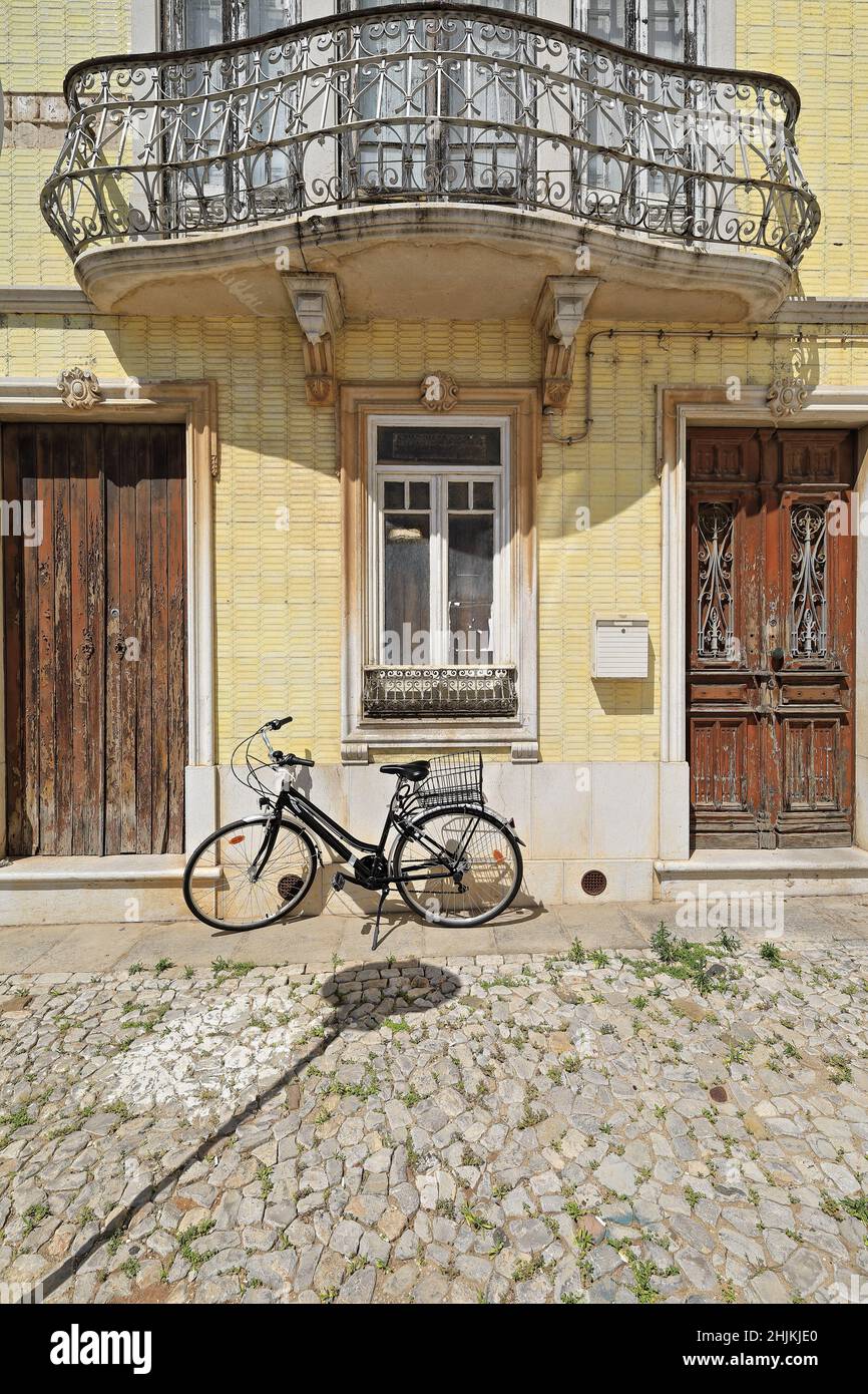 Facciata piastrellata gialla-casa cittadina neoclassica-porte in legno scheggiate-ringhiera in metallo balcone-bicicletta nera. Tavira-Portogallo-068 Foto Stock