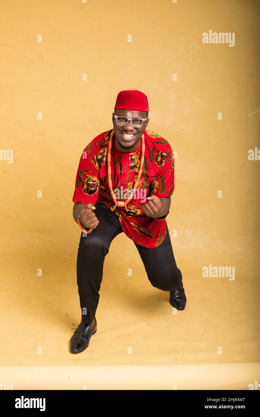 Igbo tradizionalmente vestito uomo d'affari in occhiali felici con una ginocchia giù Foto Stock