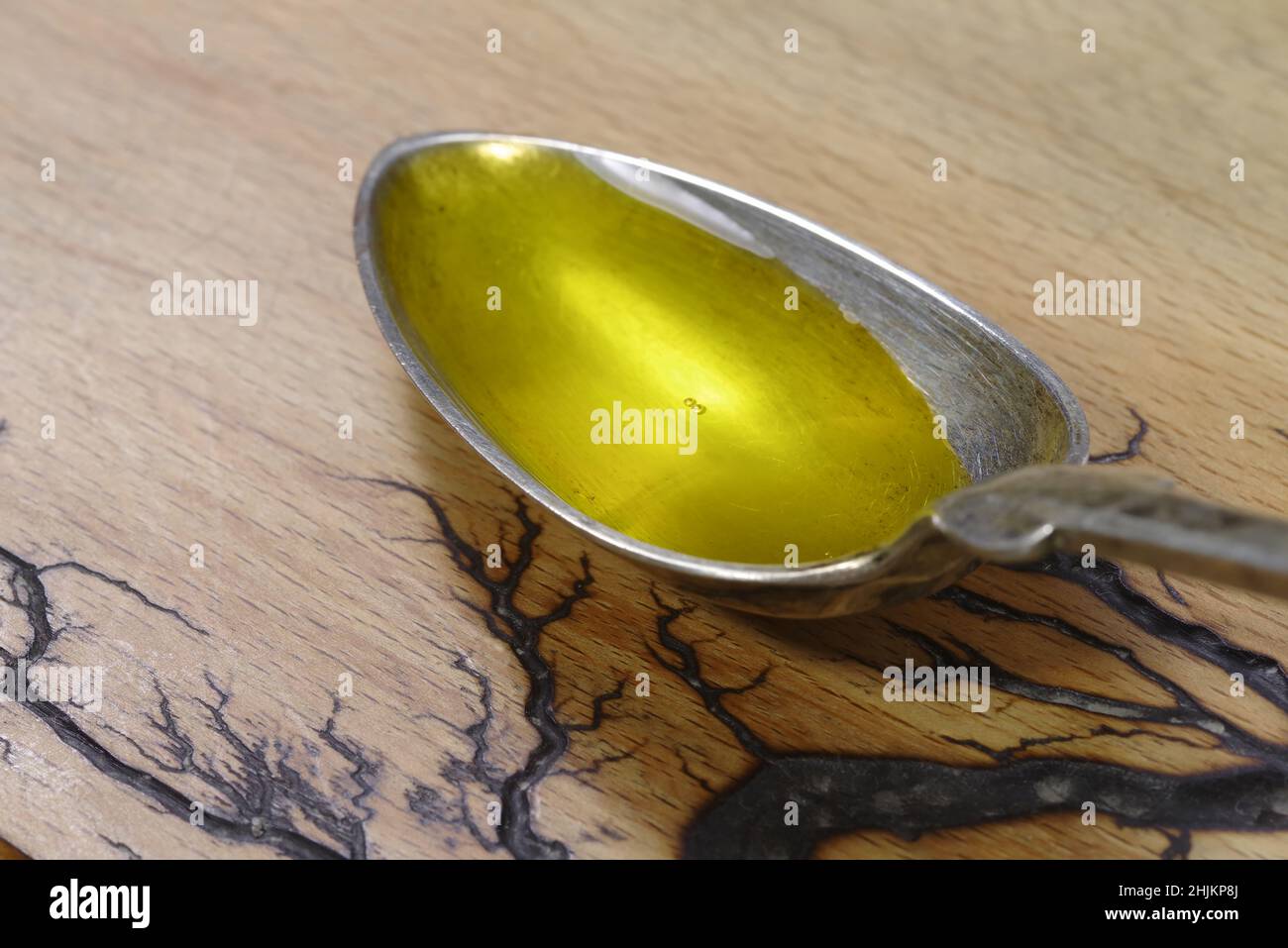 Versare l'olio di pesce in un cucchiaio di metallo su sfondo di legno. Omega 3 vitamine in primo piano cucchiaio Foto Stock