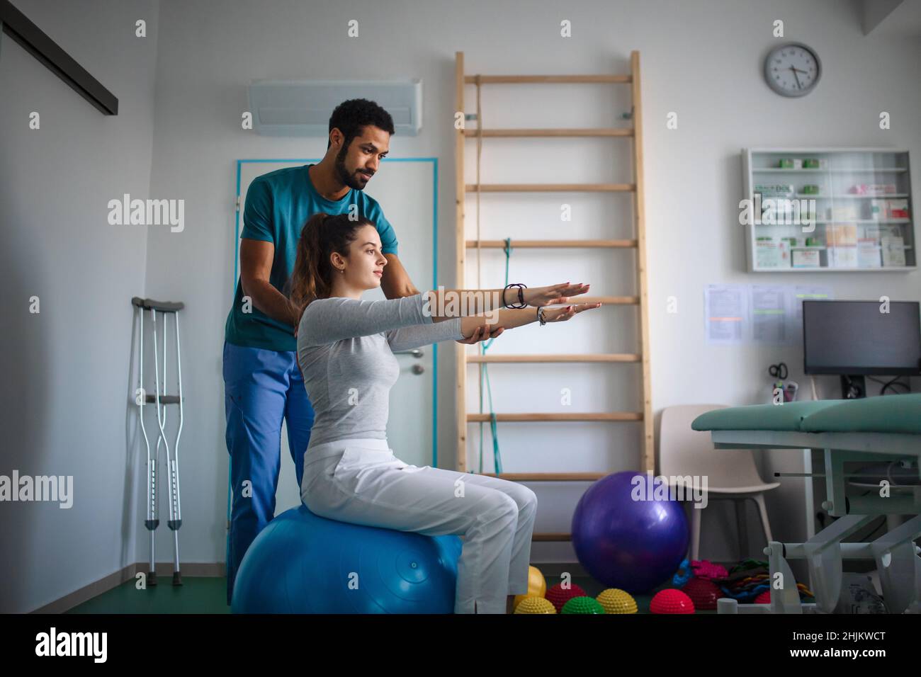 Giovane fisioterapista maschile che si esercita con una giovane paziente in una stanza fisica Foto Stock