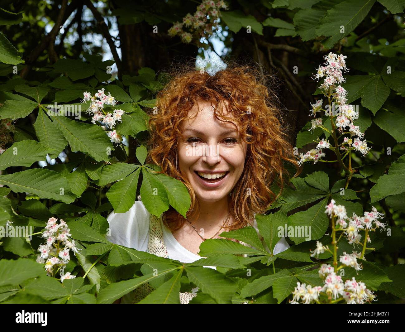 Ritratto di bella donna capelli rossi con sorriso raggiante tra i fiori di castagno. Foto Stock