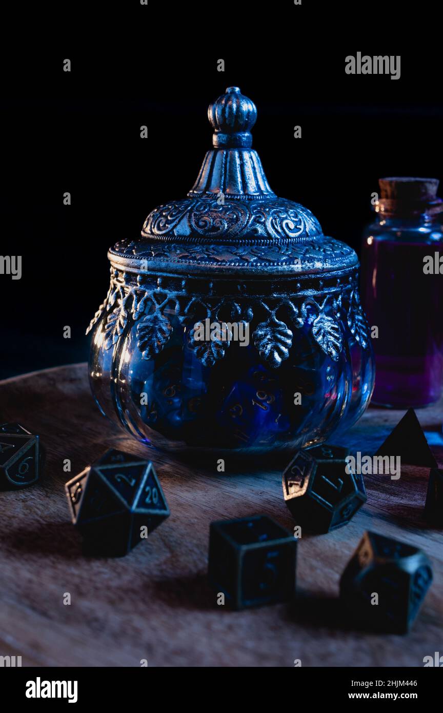 Immagine verticale di una pentola ornata in vetro piena di dadi di gioco di ruolo blu su un piatto di legno Foto Stock