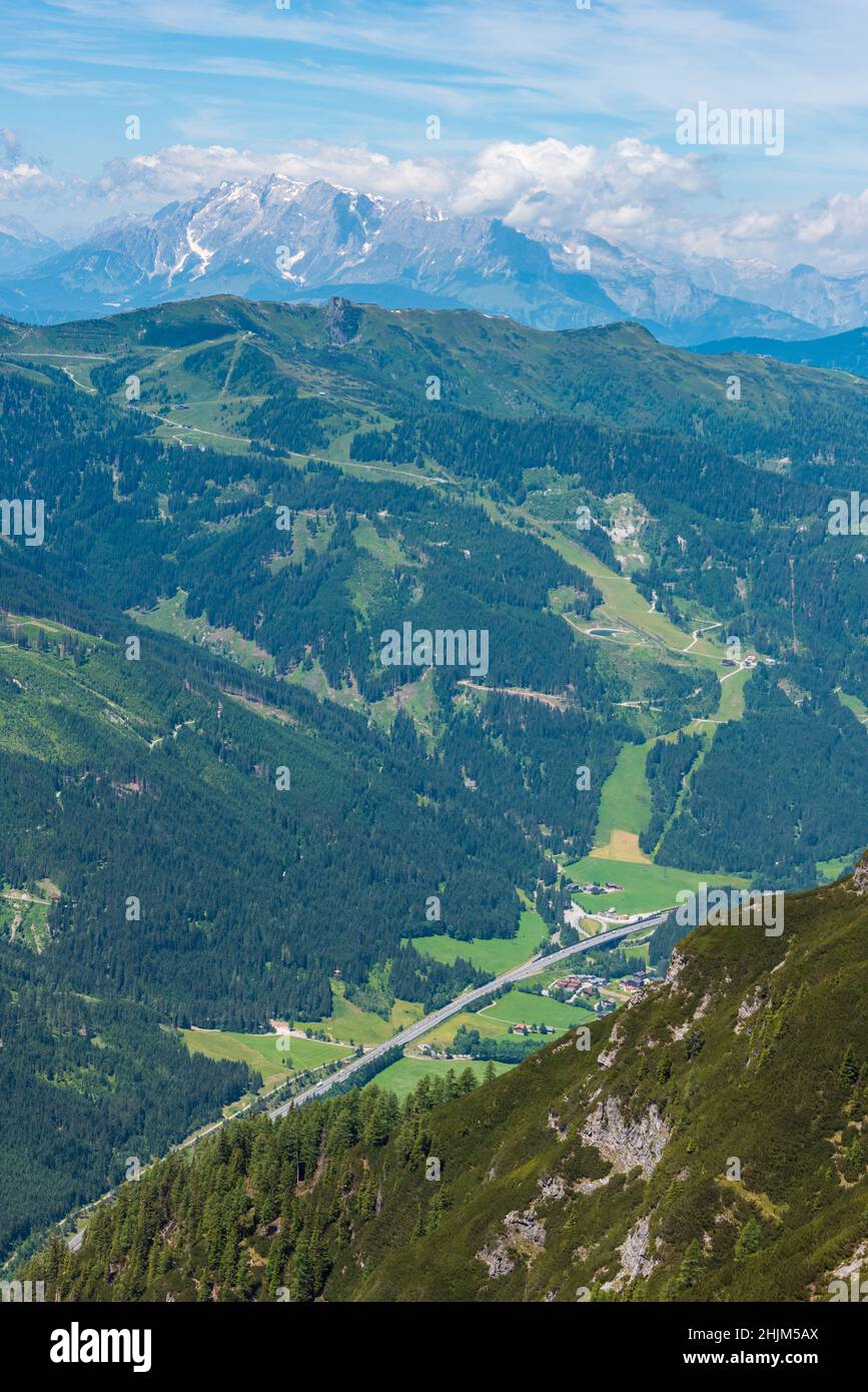 L'autostrada tra le alpi visto dall'alto. Le montagne sono coperte di alberi e arbusti, e in fondo si trova una strada asfaltata e bianca li Foto Stock