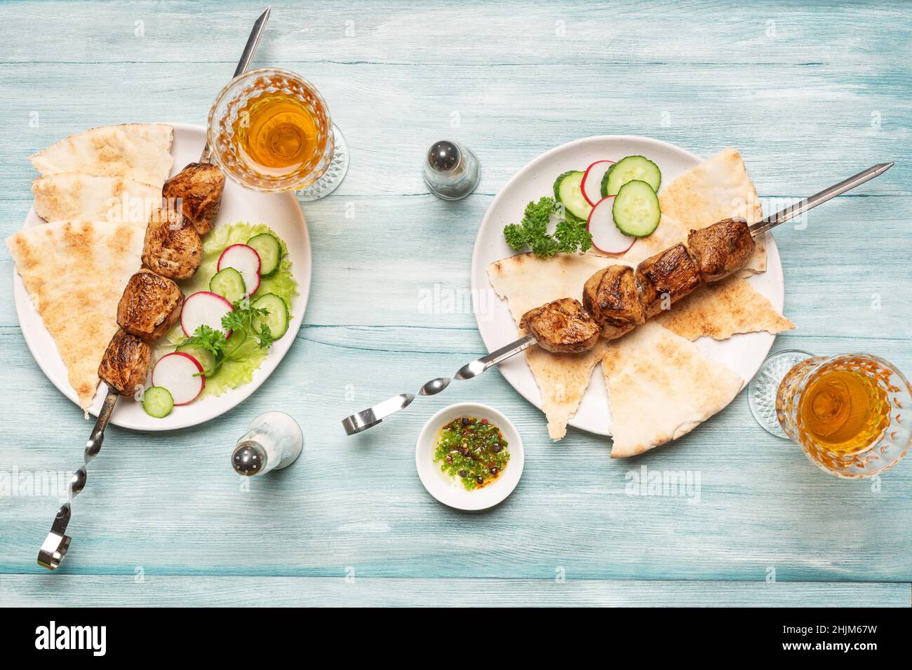 Due porzioni di appetitoso kebab shish fatto in casa, cetrioli e ravanelli tagliati a fette, bicchieri di vino vista dall'alto su sfondo blu di legno. Foto Stock