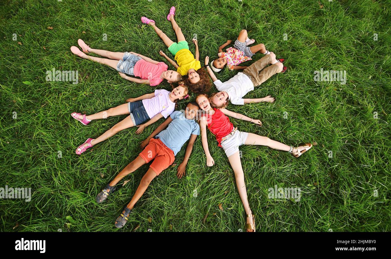 i bambini di razze e nazionalità diverse si trovano sull'erba in abiti colorati e sorridono. Foto Stock