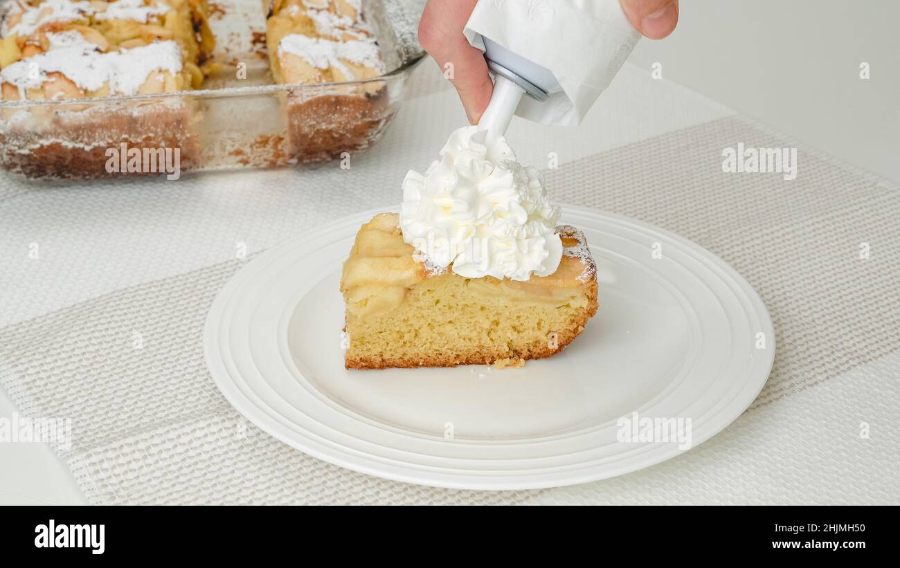 Guarnire la torta di mele con la panna montata. Fetta di torta di mele appena sfornata con base di biscotti e mele affettate da vicino su un piatto Foto Stock