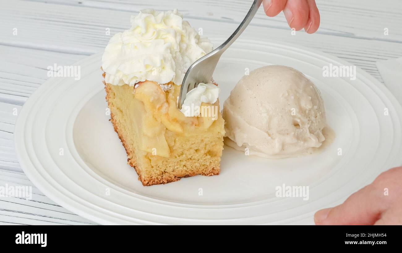 Fetta di torta di mele appena sfornata con biscotto base e mele affettate e panna montata condita con gelato alla vaniglia da vicino su un piatto su un piatto Foto Stock