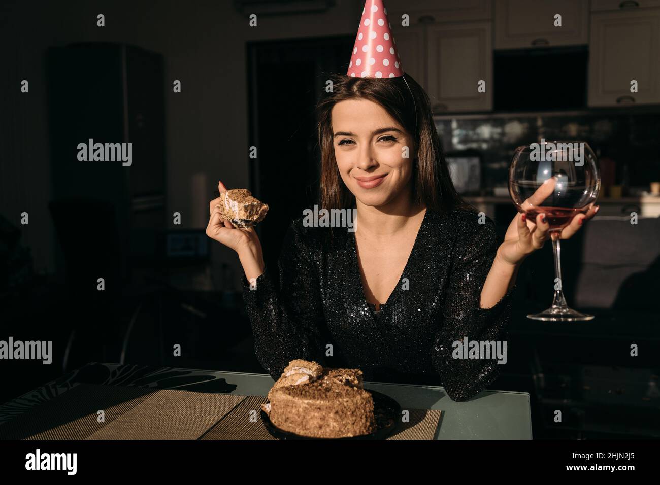 Festa di compleanno a distanza, bella donna caucasica che tiene un bicchiere di vino e mangiare torta di compleanno in appartamento, concetto di festa di compleanno Foto Stock