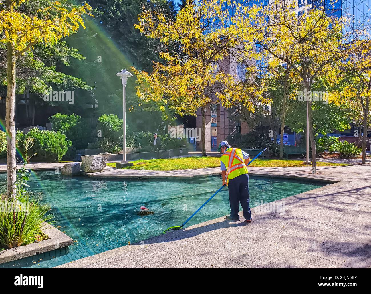 Il lavoratore che pulisce la fontana dalle foglie. I servizi della città puliscono la fontana. L'uomo lavora in autunno Foto Stock