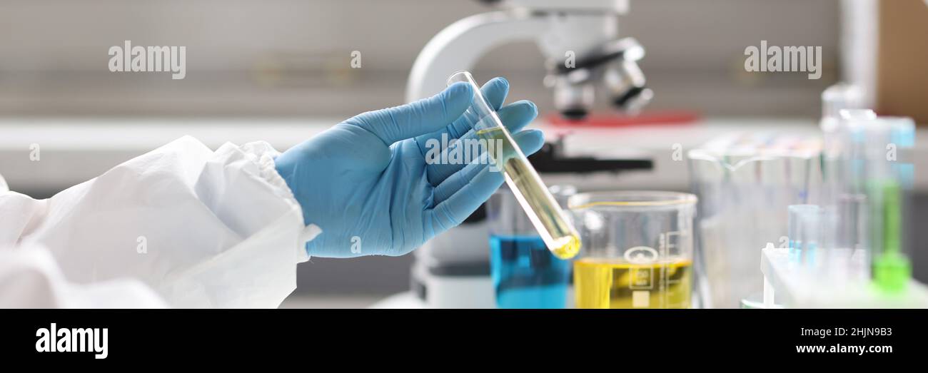 Lo scienziato con guanti può contenere provette con liquido trasparente e tipi sulla tastiera Foto Stock