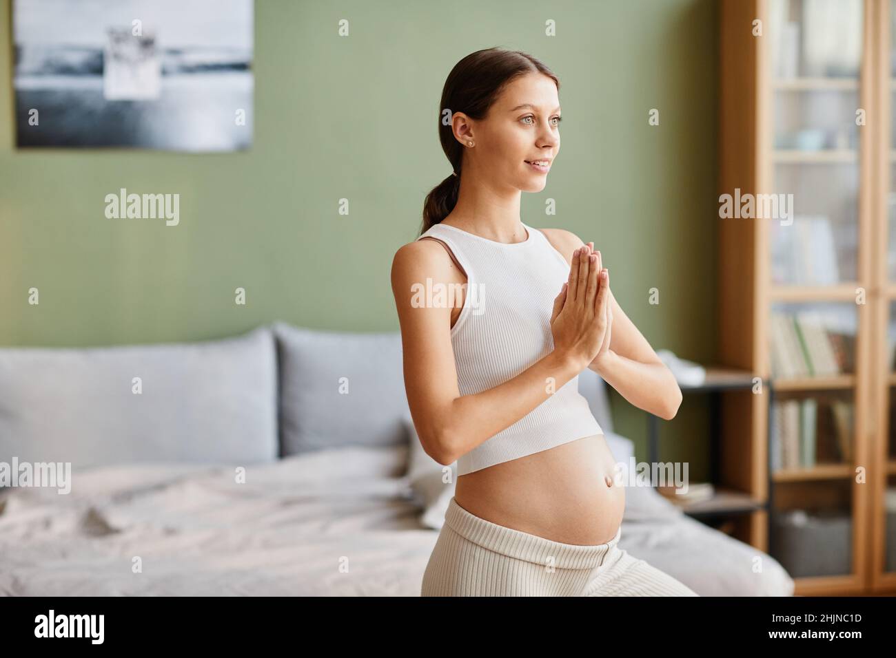 Giovane donna incinta che fa gli esercizi di yoga durante l'allenamento al mattino a casa Foto Stock