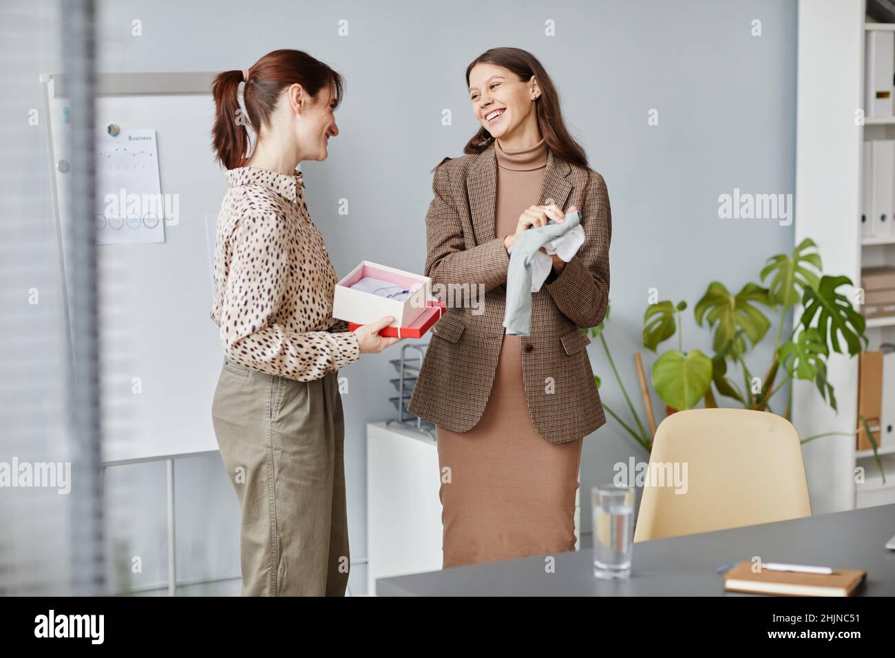 Donna d'affari felice incinta che ottiene il regalo dal suo collega e sorridente mentre si levano in piedi alla stanza del consiglio Foto Stock