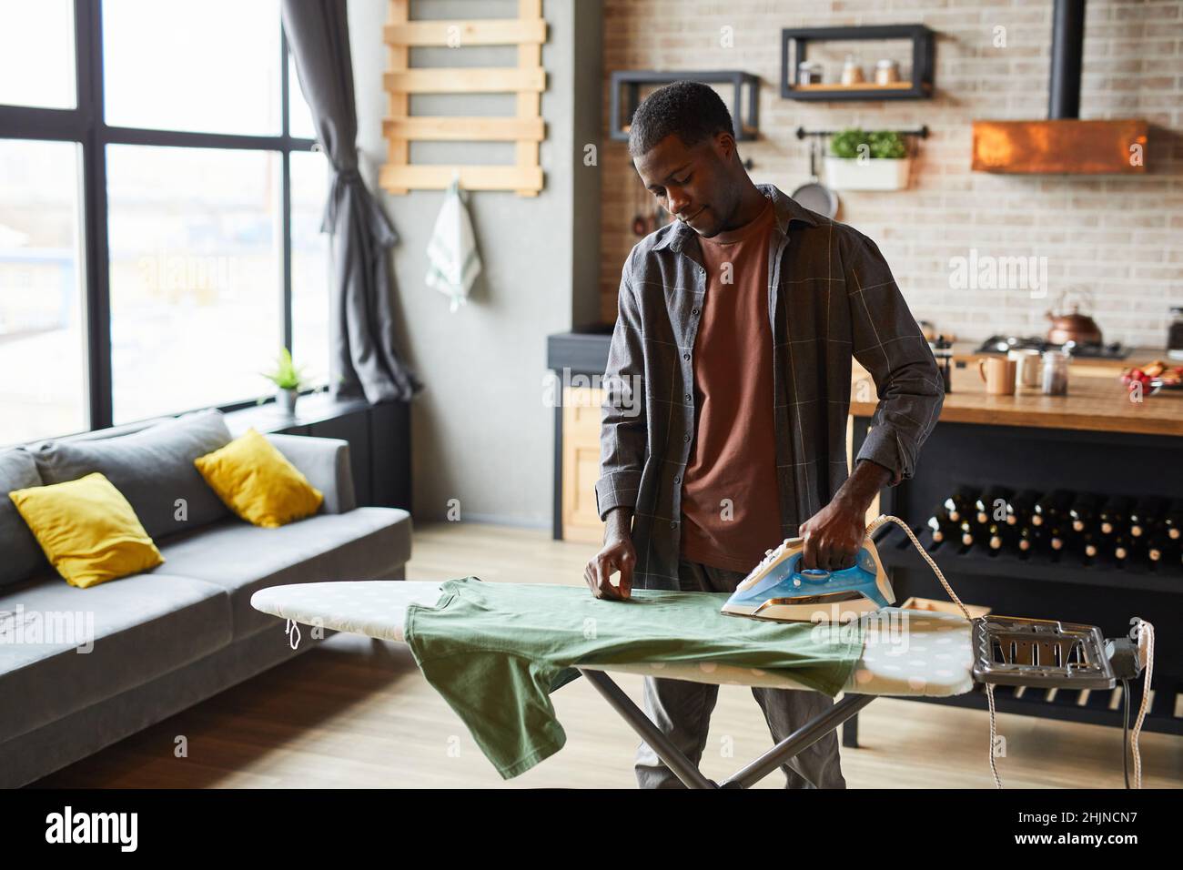 Ritratto di giovane uomo afro-americano stirare vestiti in studio appartamento, stile di vita di bachelor e concetto di famiglia chores, spazio copia Foto Stock